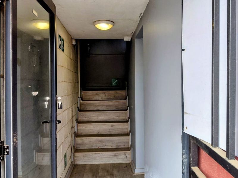 A functional industrial hallway featuring a staircase with wood-look treads, exposed brick walling, and a ceiling-mounted light fixture.