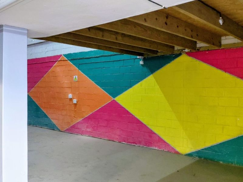 An open utility or storage space featuring exposed timber ceiling joists and vibrant geometric painted concrete block walls.