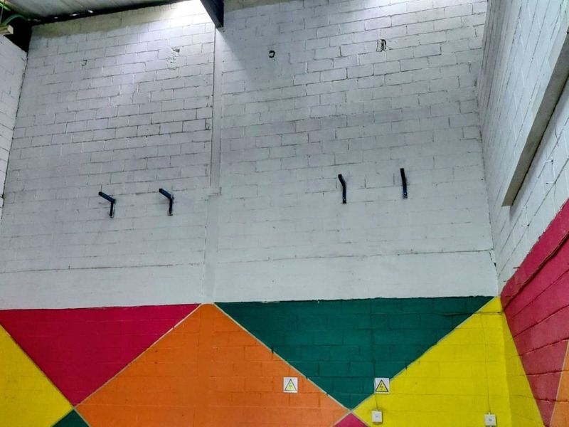 An industrial utility space featuring high ceilings, exposed painted brickwork, and wall-mounted brackets, suitable for various commercial or storage applications.