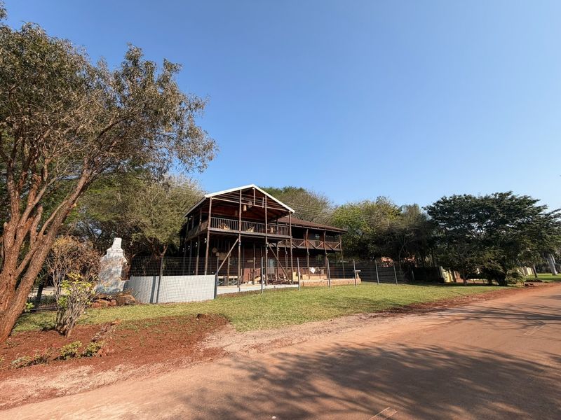 A two-story timber-clad house featuring wrap-around balconies, set behind a wire mesh fence with a clear view from the street.