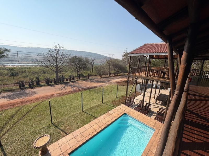 Elevated view of a swimming pool with a tiled surround, wooden decking, and a covered patio area overlooking the surrounding landscape.