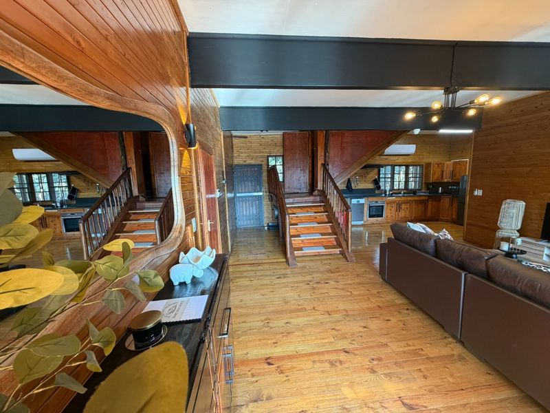 Spacious open-plan living area featuring warm timber wall cladding, exposed structural beams, timber flooring, and a functional kitchen with integrated appliances.