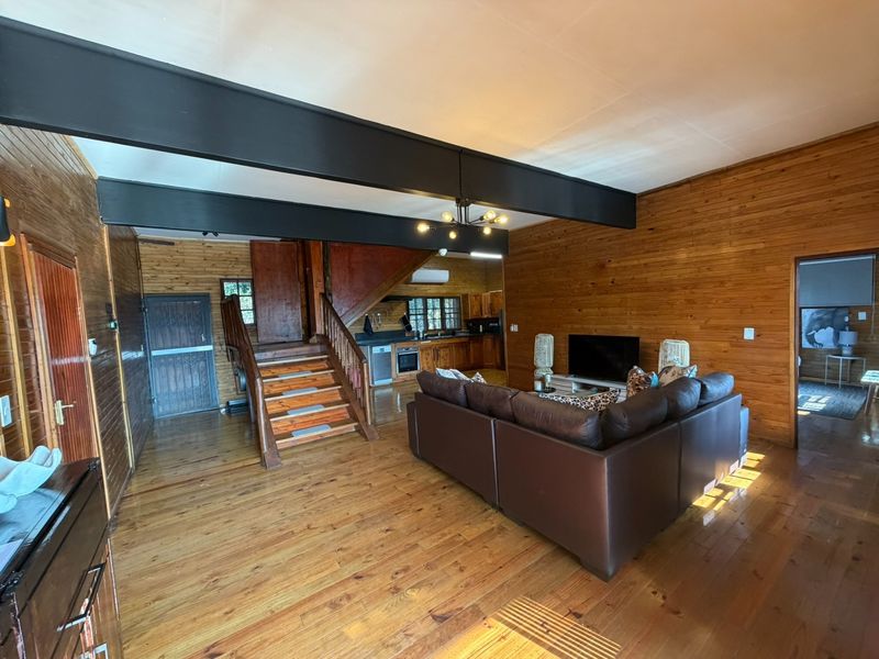 Open-plan living area featuring timber wall paneling, exposed steel beams, and a timber staircase, seamlessly connecting to a functional kitchen space.