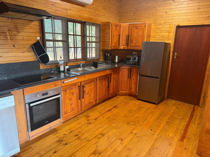 A rustic kitchen featuring warm wooden wall paneling, cabinetry, and flooring, complemented by granite countertops and integrated stainless steel appliances.