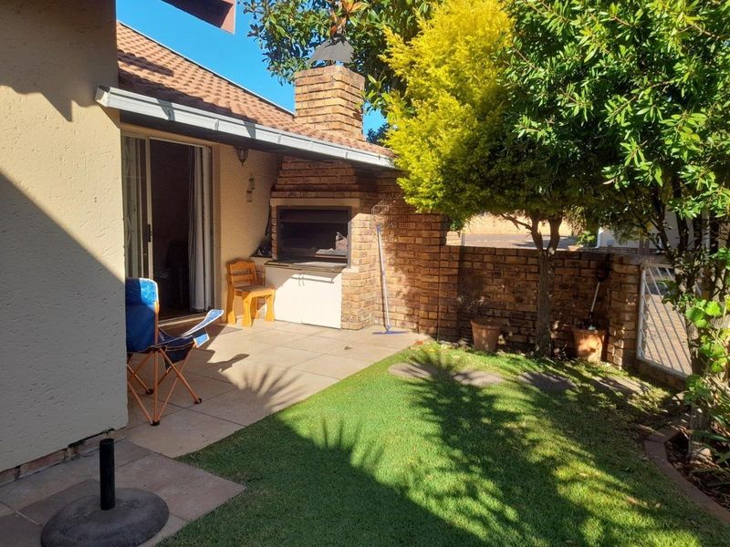 A private patio area featuring a built-in brick braai, tiled flooring, and direct access to a small garden space through sliding glass doors.