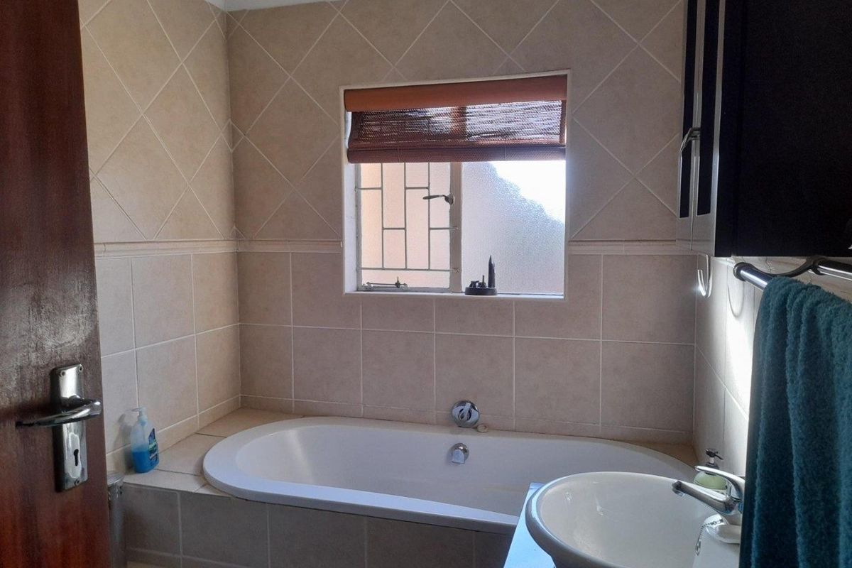 A functional bathroom featuring a built-in bathtub, a modern vessel sink, and neutral wall tiling with a window for natural light.