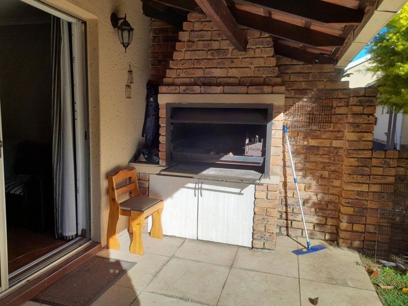 Covered patio area featuring a built-in brick braai and fireplace, tiled flooring, and direct access to the interior via a sliding door.