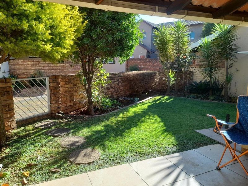 A covered patio area overlooking a private garden with a lawn, established trees, and brick boundary walls.