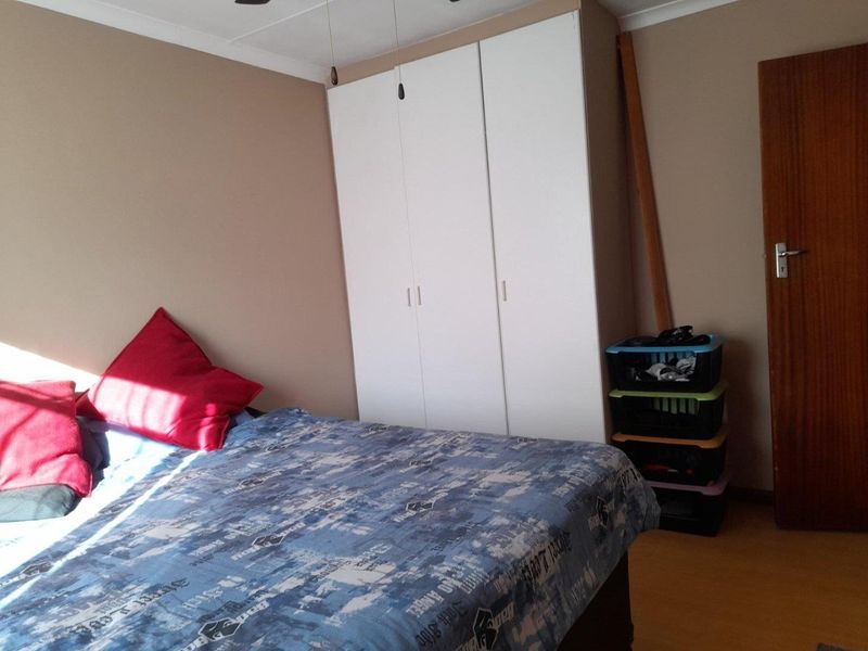 A bedroom featuring a built-in wardrobe, wooden door, and ceiling fan, providing functional storage and basic amenities.