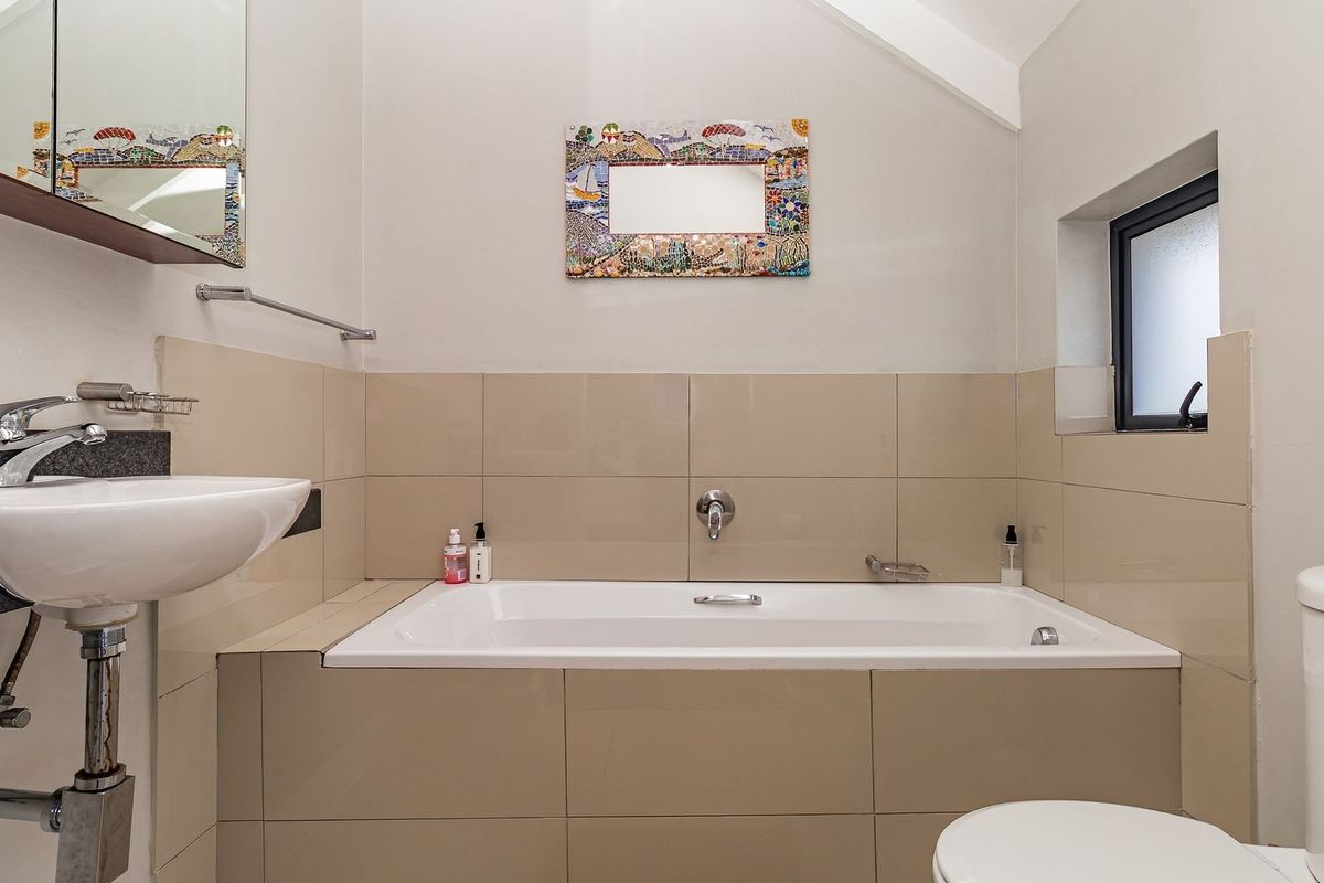 A functional bathroom featuring a built-in bathtub, wall-mounted basin with chrome fixtures, and neutral wall tiling.