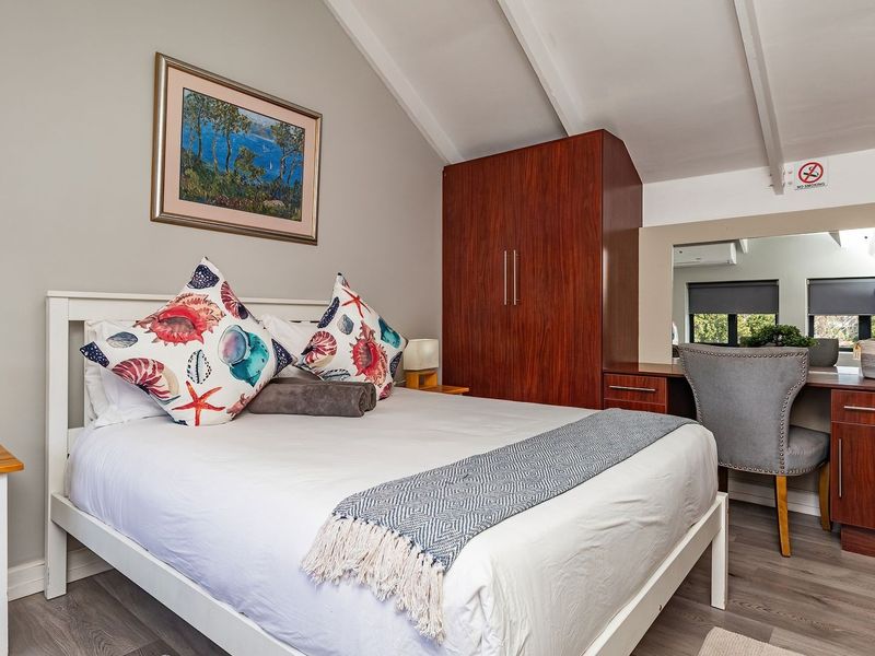 A well-maintained bedroom featuring a vaulted ceiling, built-in wooden wardrobe, and integrated vanity unit with laminate flooring.