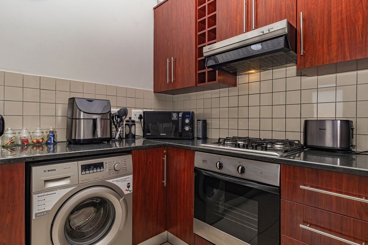 Compact kitchen featuring cherry wood cabinetry, granite countertops, tiled backsplash, and integrated appliances including a gas hob, oven, and washing machine.