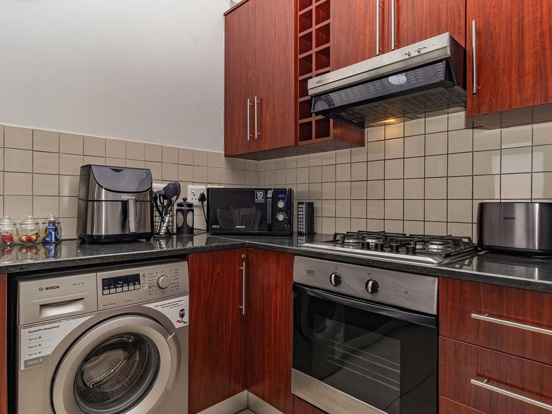 Compact kitchen featuring cherry wood cabinetry, granite countertops, tiled backsplash, and integrated appliances including a gas hob, oven, and washing machine.