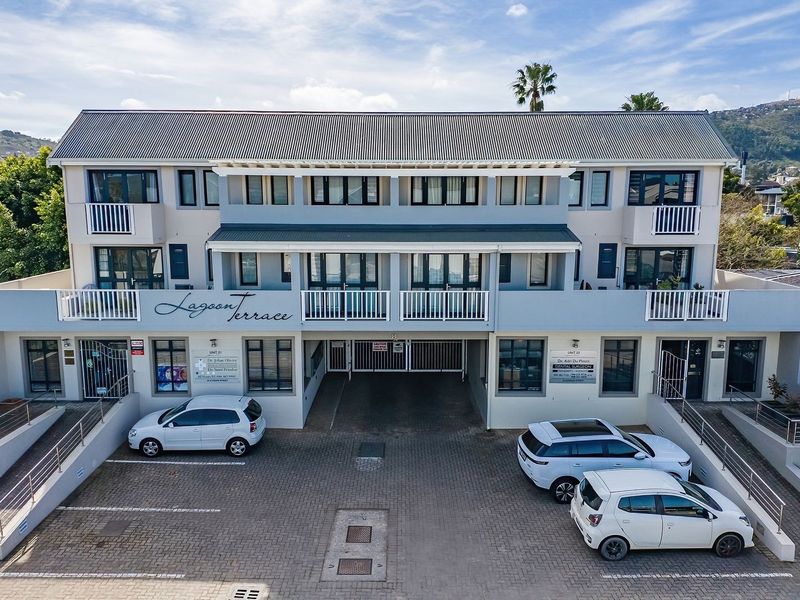 Front elevation of Lagoon Terrace apartment complex featuring a paved driveway, secure gated access, and multiple balconies with metal railings.