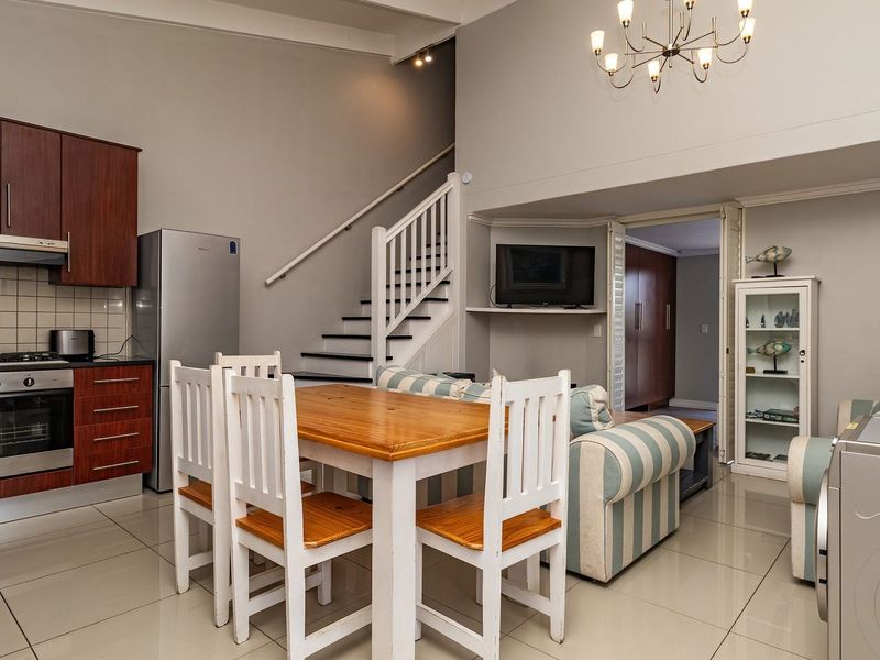 Open-plan living and kitchen area featuring tiled flooring, built-in cabinetry with integrated appliances, and a staircase leading to the upper level.
