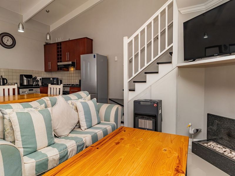 Open-plan living area featuring a kitchen with wood cabinetry, a fireplace, and a staircase leading to an upper level.