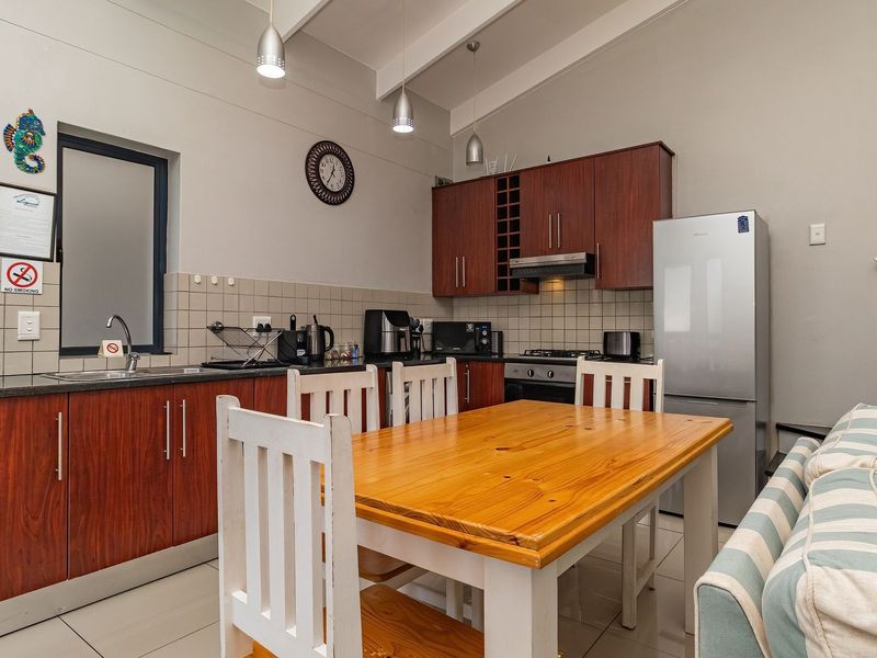 Open-plan kitchen and dining area featuring wood-finish cabinetry, tiled flooring, and integrated appliances, creating a functional and cohesive living space.