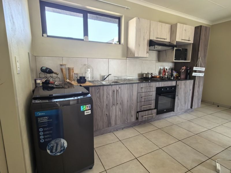A functional kitchen featuring modern wood-grain cabinetry, built-in oven with extractor fan, tiled backsplash, and neutral floor tiles.