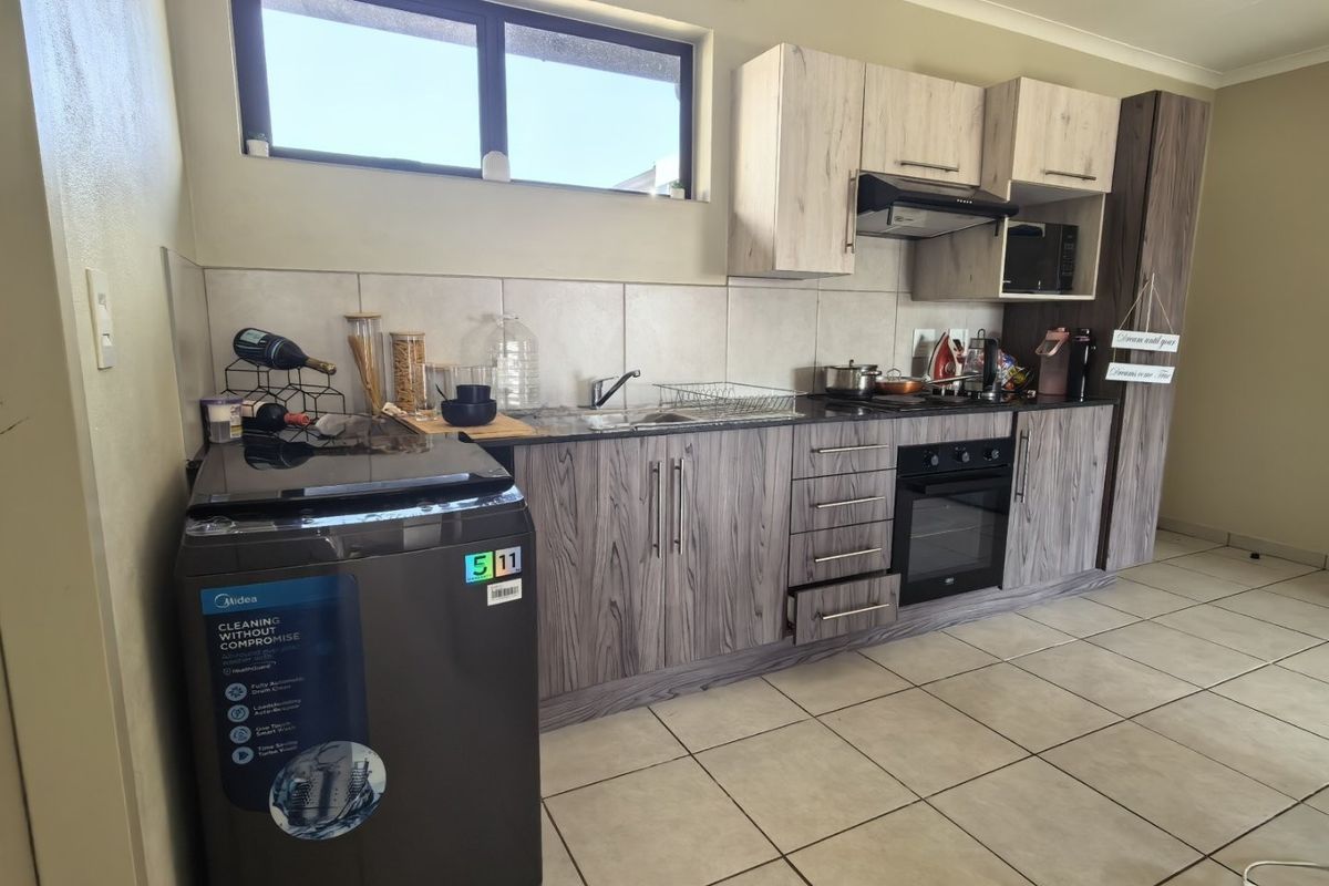 A functional kitchen featuring modern wood-grain cabinetry, built-in oven with extractor fan, tiled backsplash, and neutral floor tiles.