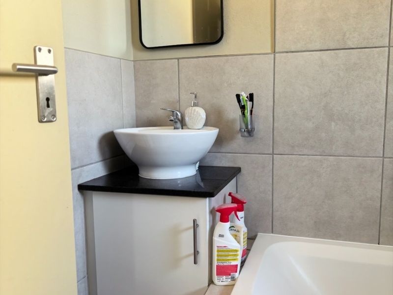 A compact bathroom featuring a modern vessel sink on a granite-topped vanity, a built-in bathtub, and neutral ceramic wall and floor tiling.