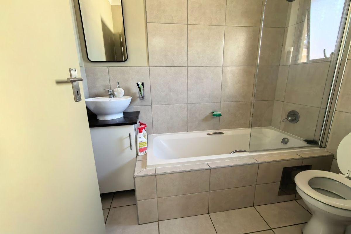 A functional bathroom featuring a vessel sink vanity, a bathtub with a glass shower screen, and neutral ceramic tiling throughout.
