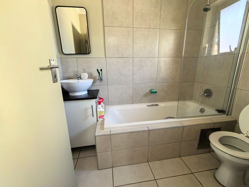 A functional bathroom featuring a vessel sink vanity, a bathtub with a glass shower screen, and neutral ceramic tiling throughout.