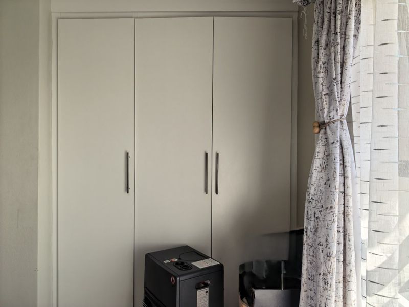 A bedroom interior featuring a clean, white built-in wardrobe with modern vertical handles.