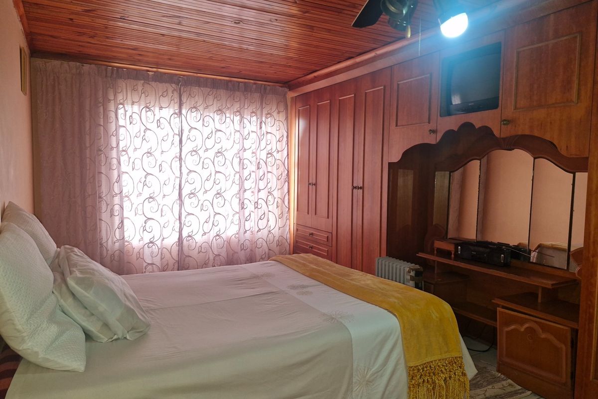 A bedroom featuring built-in wooden cupboards, a timber-clad ceiling, and a ceiling fan, offering a traditional aesthetic with tiled flooring.