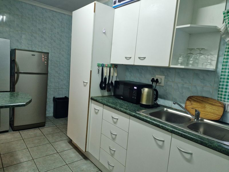 A functional kitchen featuring white cabinetry, green laminate countertops, a stainless steel double sink, and light blue tiled wall finishes.