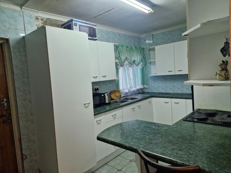 A functional kitchen featuring laminate countertops, built-in cabinetry, and a double bowl sink, offering potential for modernization and cosmetic updates.