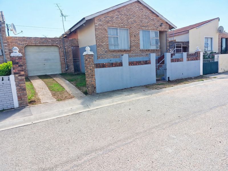 Front view of a single-story brick house featuring a garage, concrete driveway, and a perimeter boundary wall.