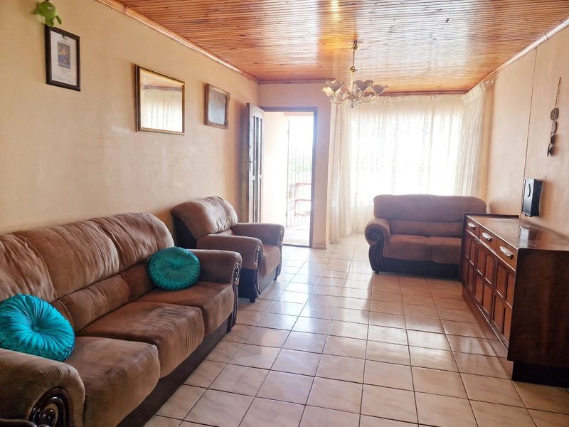 A living room featuring a timber tongue and groove ceiling, ceramic tiled flooring, and a chandelier, with access to an outdoor area.