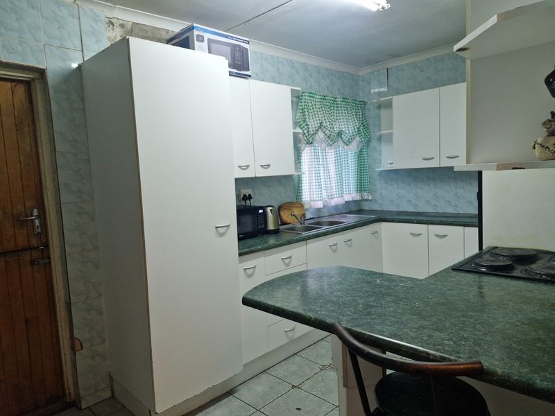 A dated kitchen featuring laminate cabinetry, green countertops, and tiled splashbacks, offering a functional layout with potential for modern renovation.