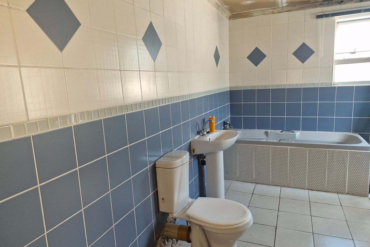 A dated bathroom featuring a pedestal basin, toilet, and built-in bathtub, currently requiring ceiling repairs and cosmetic updates to the tiling and fixtures.