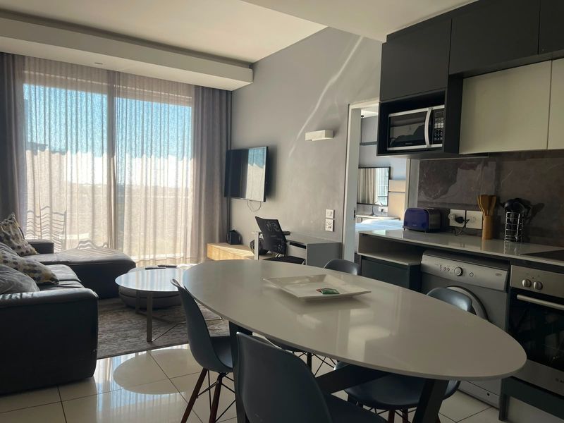 Modern open-plan living area featuring a sleek kitchen with built-in appliances, tiled flooring, and a large sliding door leading to natural light.