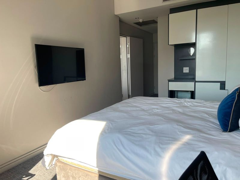 A modern bedroom featuring built-in cabinetry, wall-mounted television, and neutral finishes, providing a clean and functional living space.
