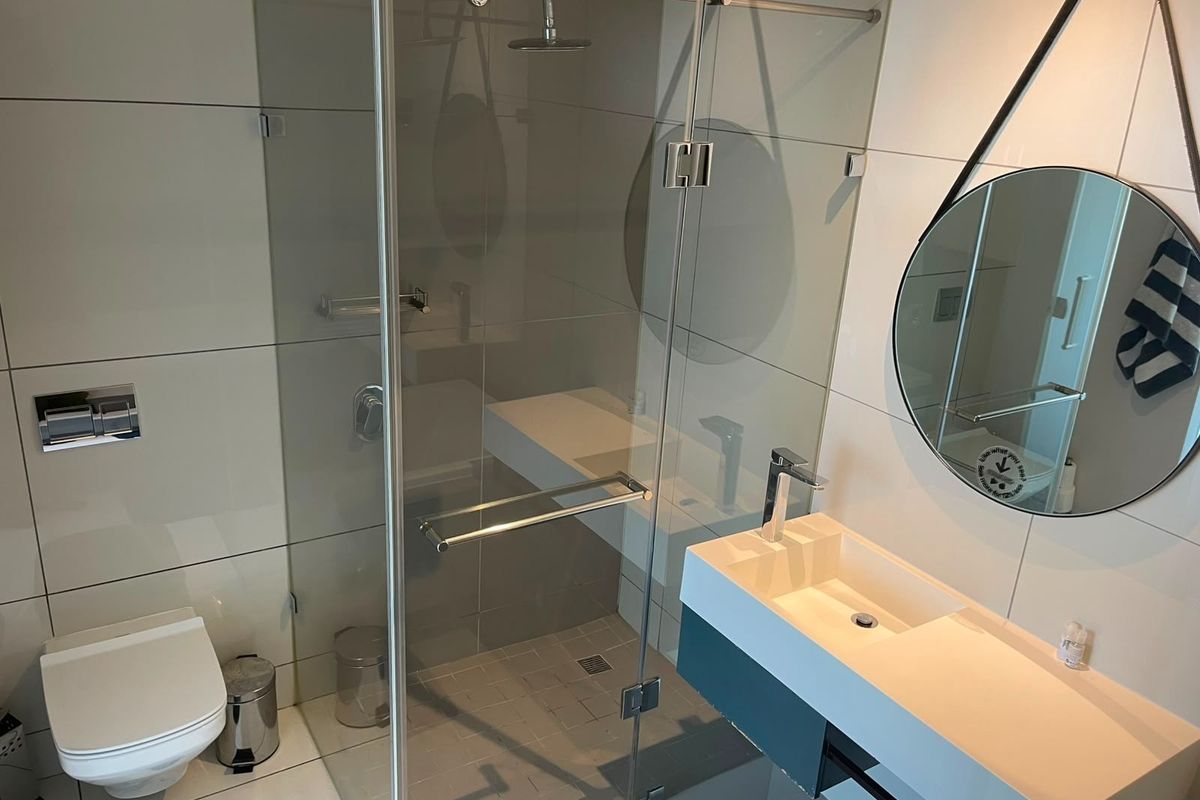 Modern bathroom featuring a wall-mounted toilet, a sleek floating vanity with basin, and a spacious glass-enclosed shower with a rain shower head.