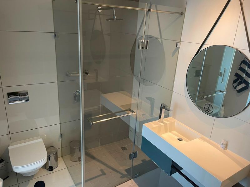 Modern bathroom featuring a wall-mounted toilet, a sleek floating vanity with basin, and a spacious glass-enclosed shower with a rain shower head.