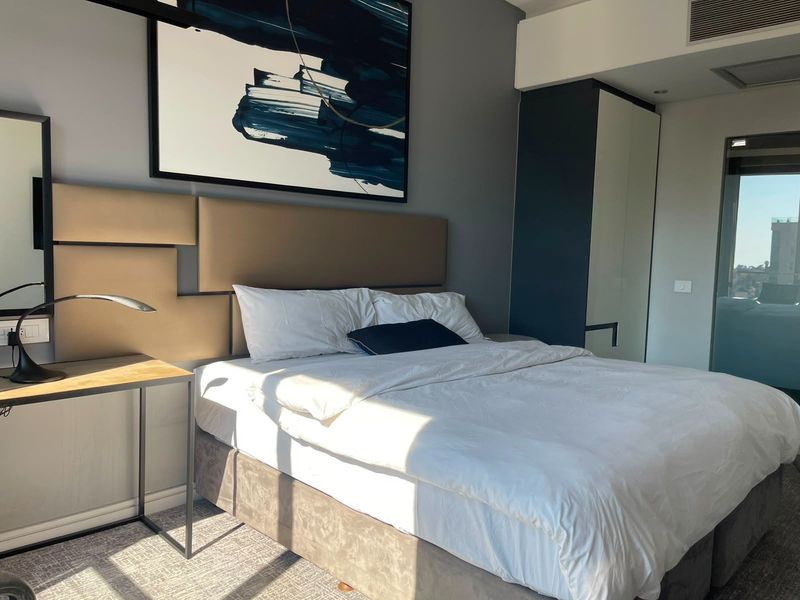 A modern bedroom featuring a built-in wardrobe, upholstered headboard, and recessed ceiling lighting, offering a clean and contemporary living space.