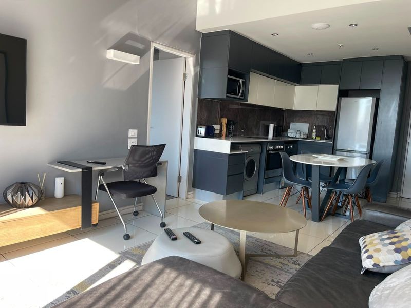 Modern open-plan living area featuring a contemporary kitchen with built-in cabinetry, integrated appliances, and sleek tiled flooring throughout the space.