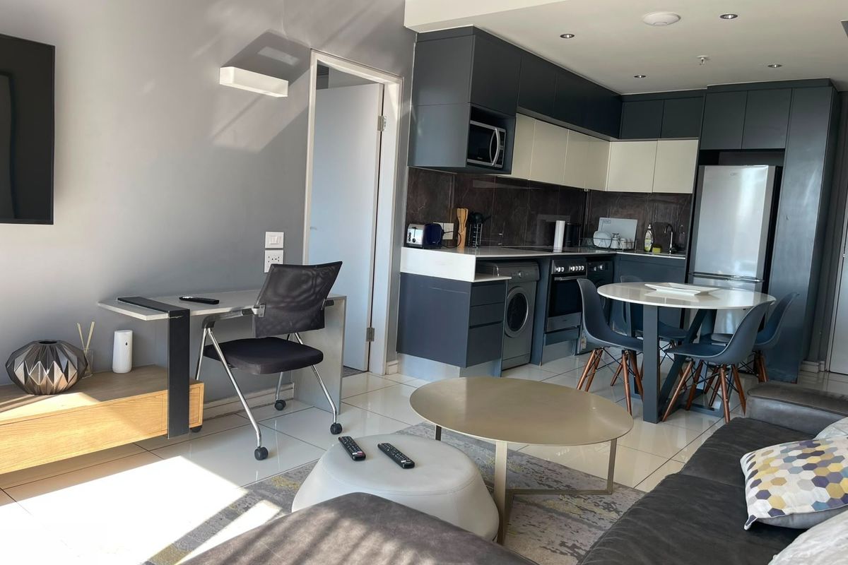 Modern open-plan living area featuring a contemporary kitchen with built-in cabinetry, integrated appliances, and sleek tiled flooring throughout the space.