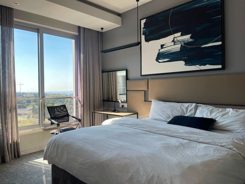 Modern bedroom featuring floor-to-ceiling windows with expansive views, integrated headboard, and contemporary recessed lighting in a well-maintained apartment setting.