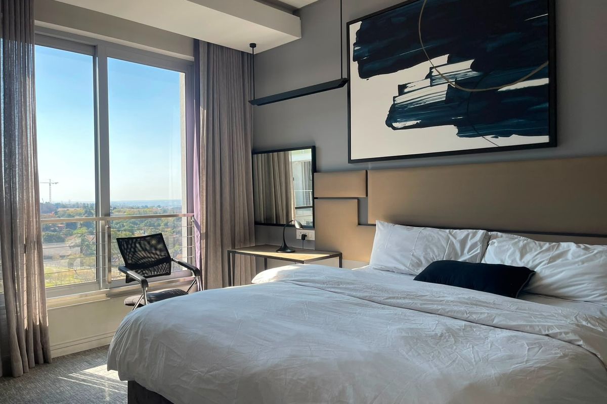 Modern bedroom featuring floor-to-ceiling windows with expansive views, integrated headboard, and contemporary recessed lighting in a well-maintained apartment setting.