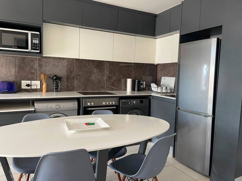 Modern kitchen featuring two-tone cabinetry, stone countertops, marble-look splashback, and integrated appliances, offering a sleek and functional cooking and laundry space.