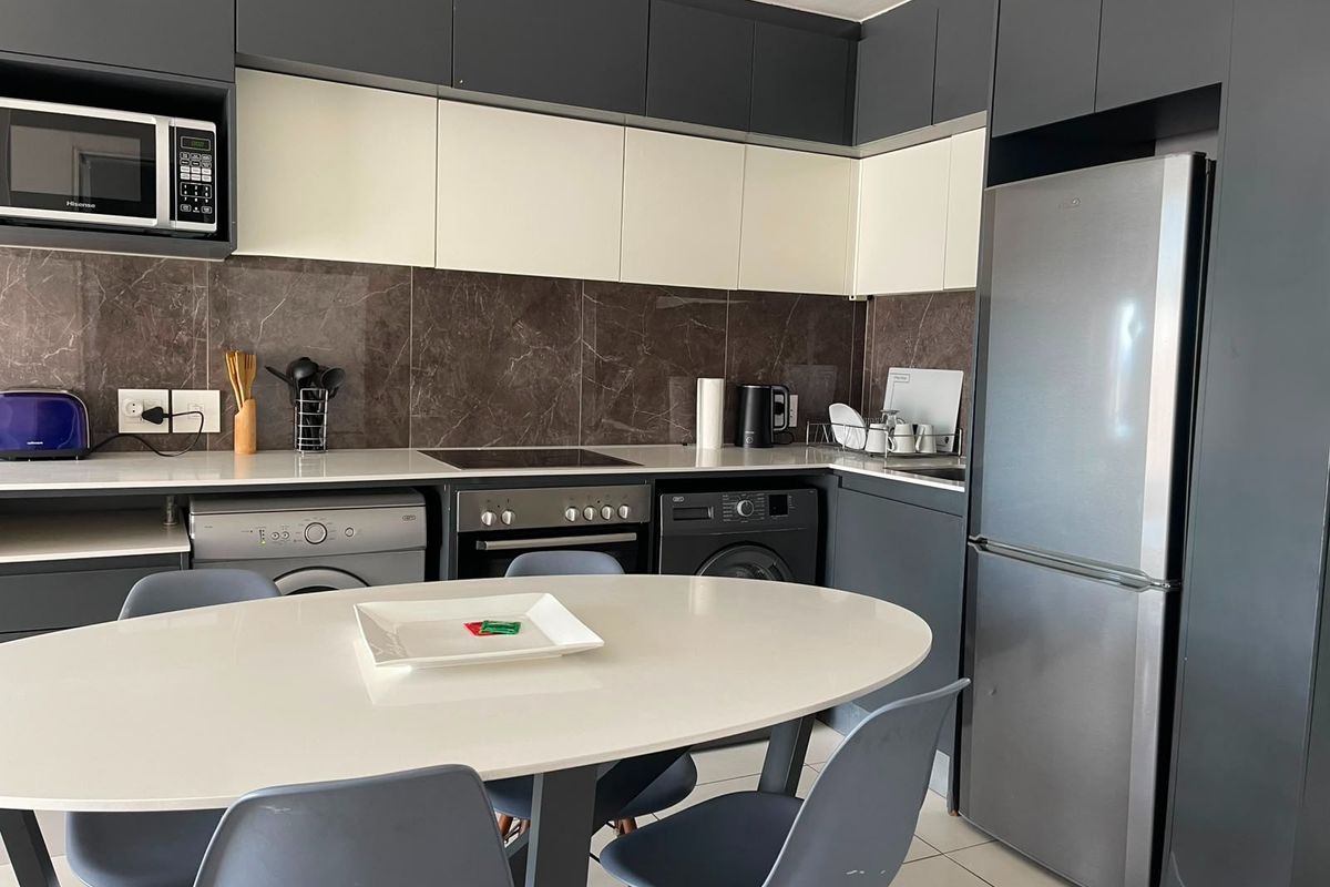 Modern kitchen featuring two-tone cabinetry, stone countertops, marble-look splashback, and integrated appliances, offering a sleek and functional cooking and laundry space.