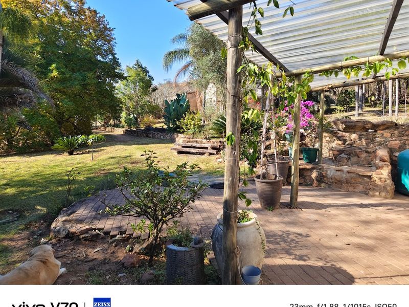 A rustic outdoor patio area featuring a timber pergola with a corrugated roof, brick paving, and a natural stone retaining wall overlooking the garden.
