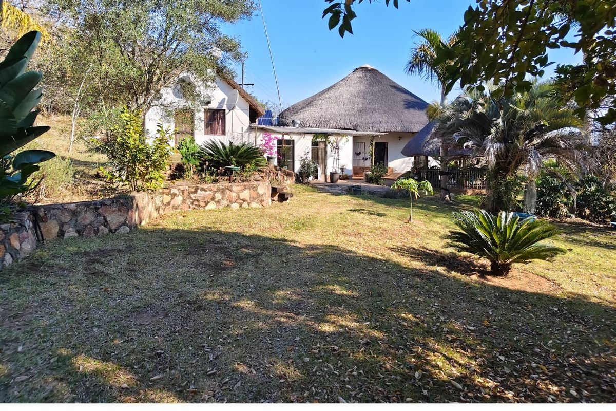 A view of the rear garden featuring a traditional thatched roof dwelling and stone retaining wall elements in a natural farm setting.