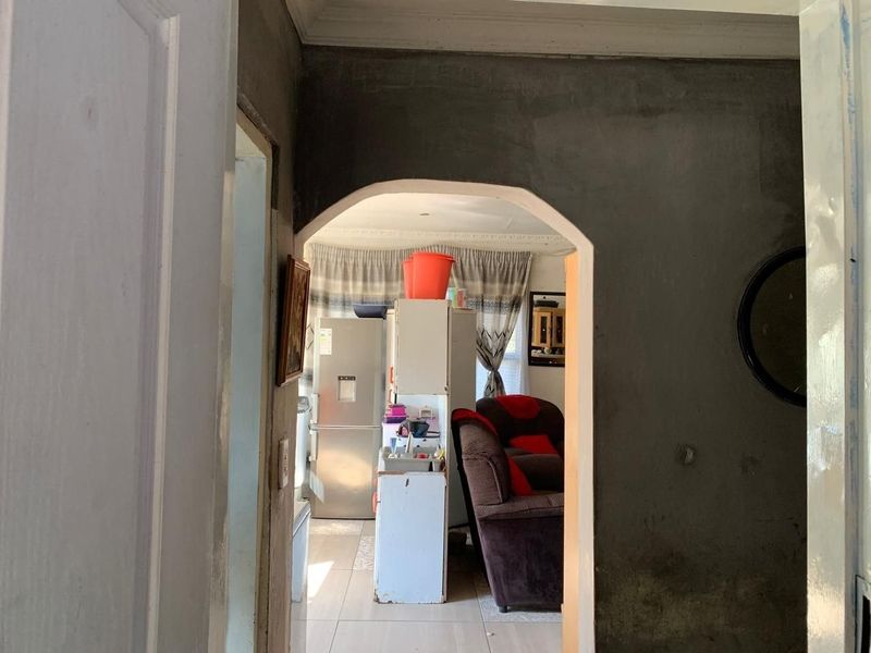 View through an arched doorway into an open plan living and kitchen area featuring tiled flooring and unfinished wall surfaces.