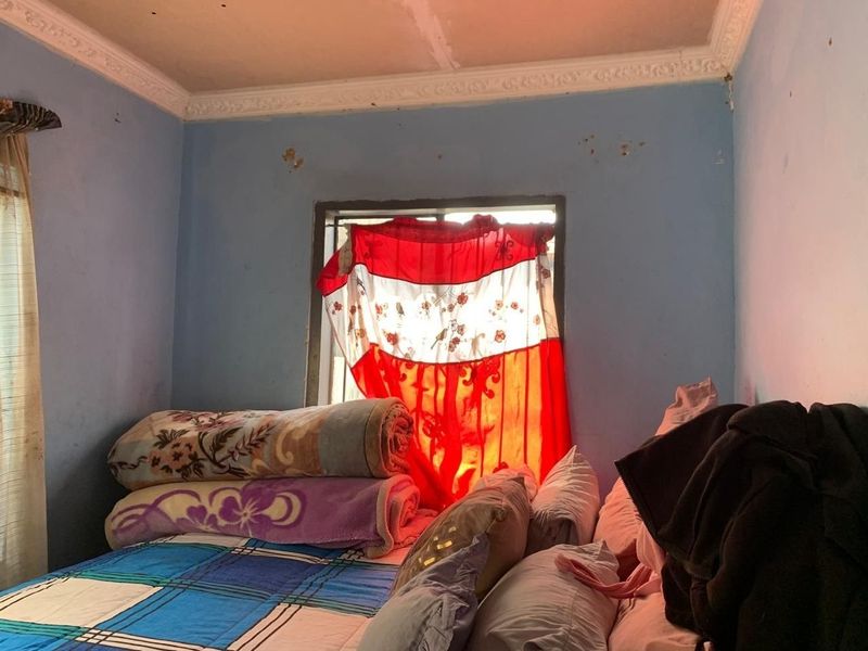 A bedroom featuring decorative ceiling cornicing and a window, currently showing signs of wall surface wear and paint deterioration.