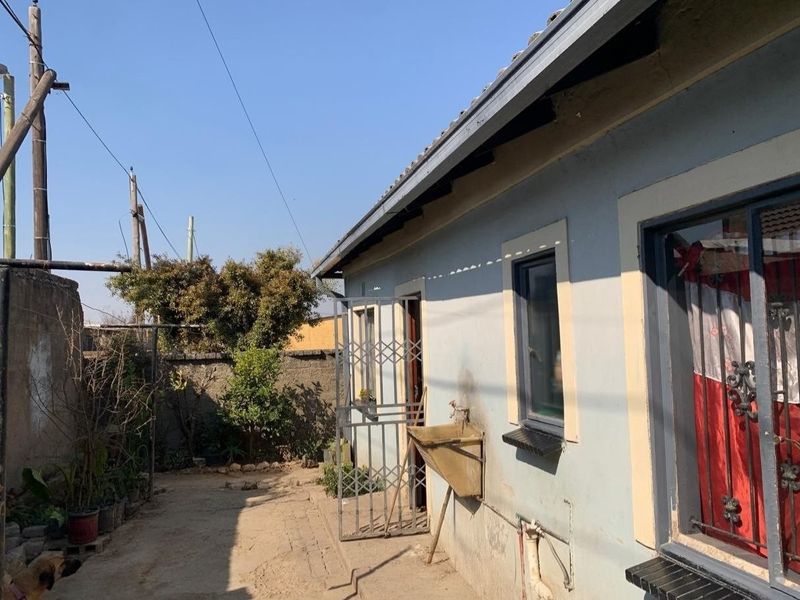 Rear exterior view of the property featuring a utility sink, security gate, and perimeter wall with visible wear to the exterior finishes.